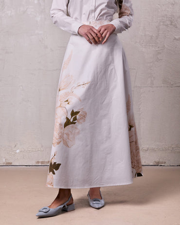 Person wearing a long white dress with floral patterns against a plain background