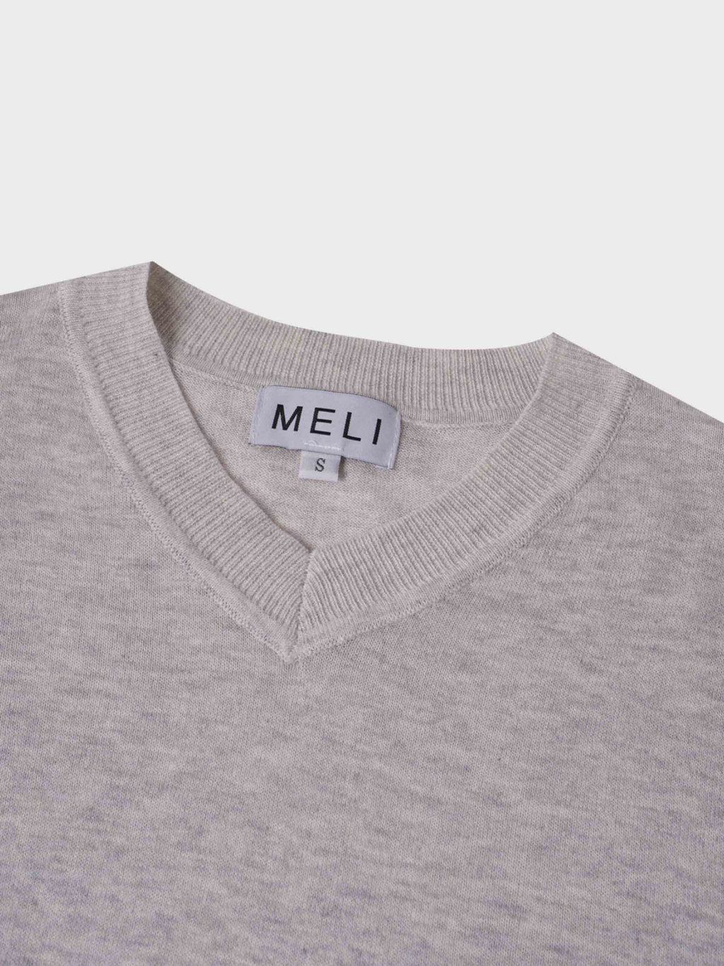 Close-up of a gray sweater with a visible brand label on a light gray background