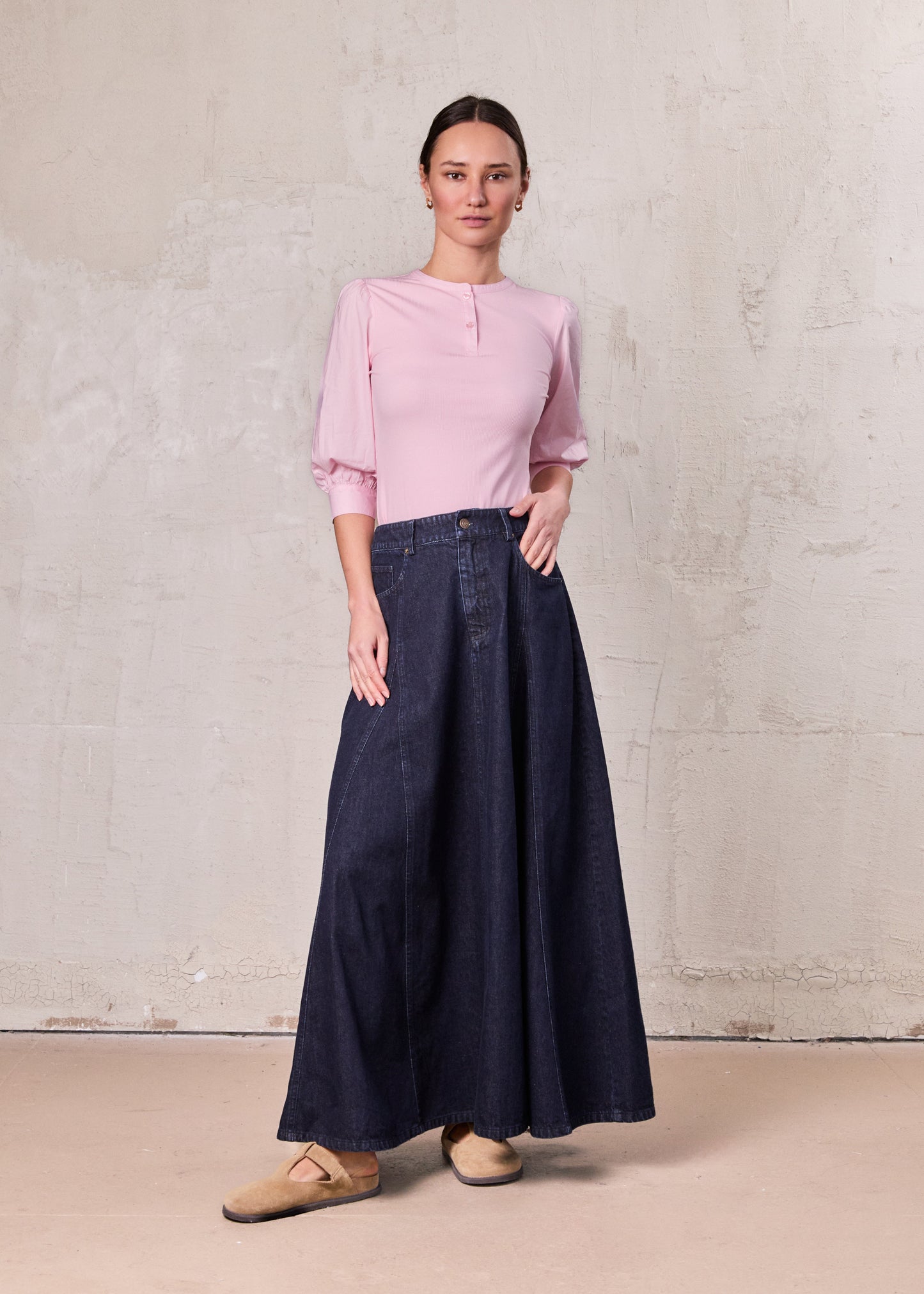 Woman wearing a pink blouse and dark blue denim skirt against a plain background