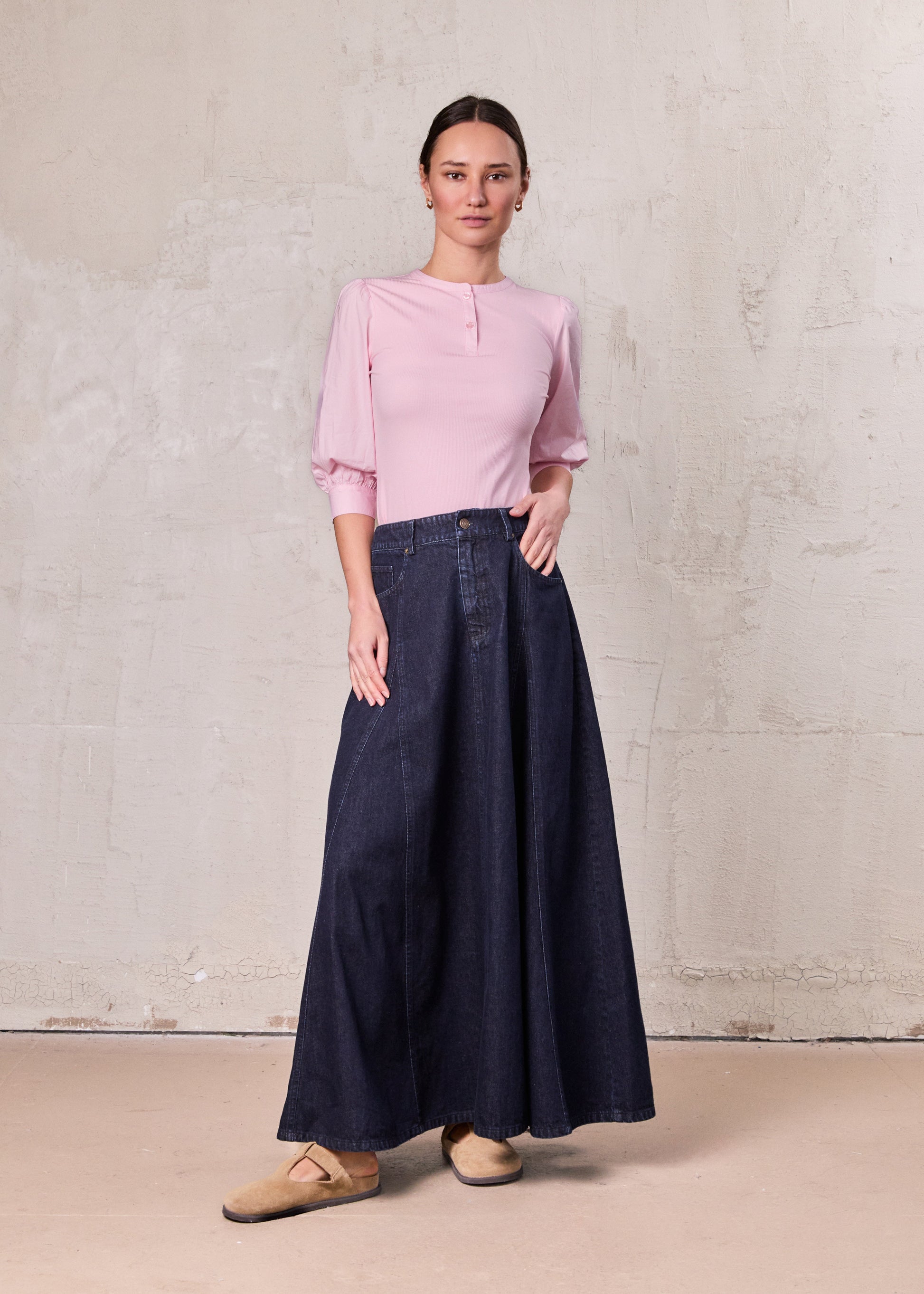 Woman wearing a pink blouse and dark blue denim skirt against a plain background