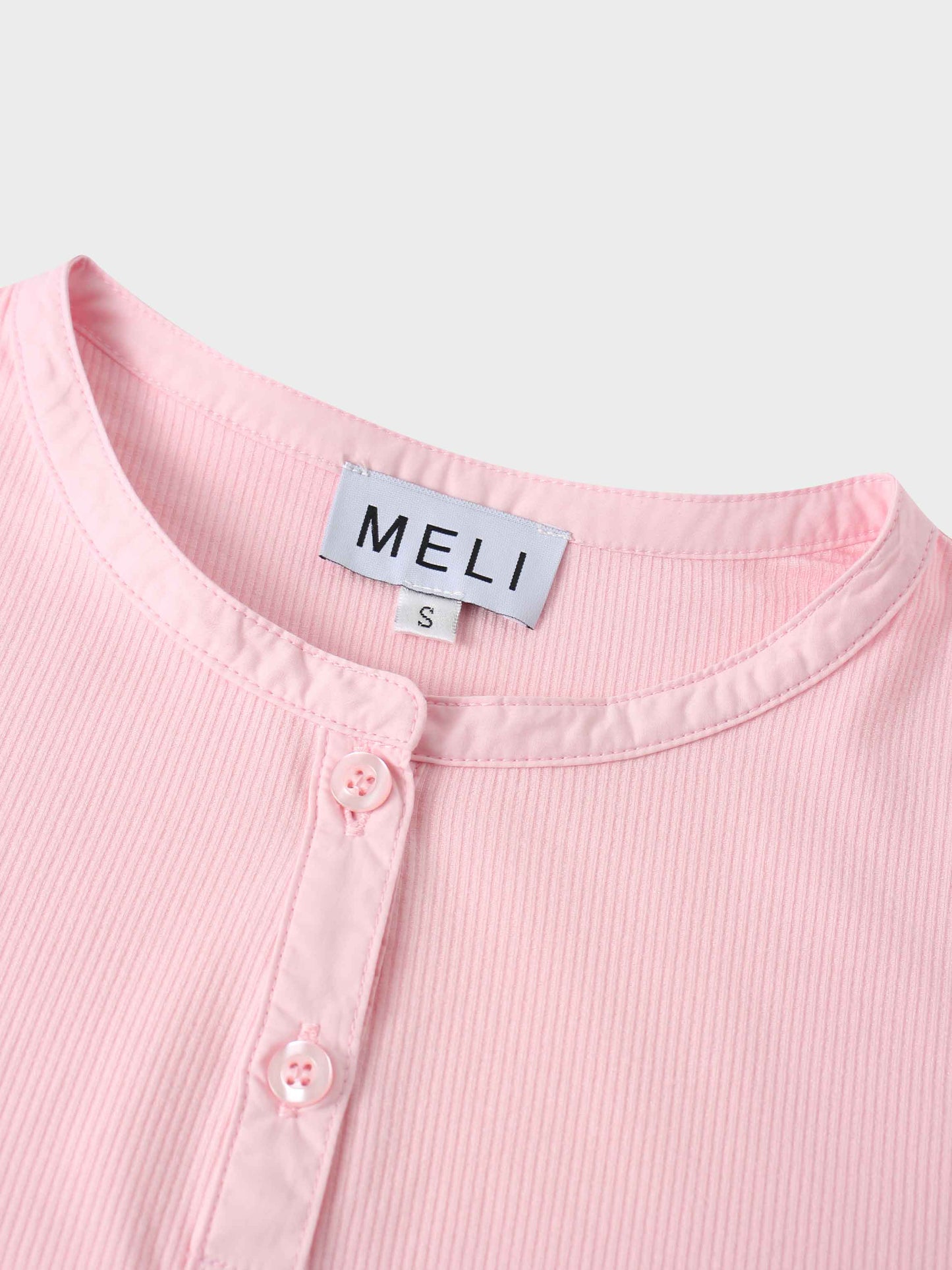 Close-up of a pink ribbed garment with 'MELI' label on a light gray background