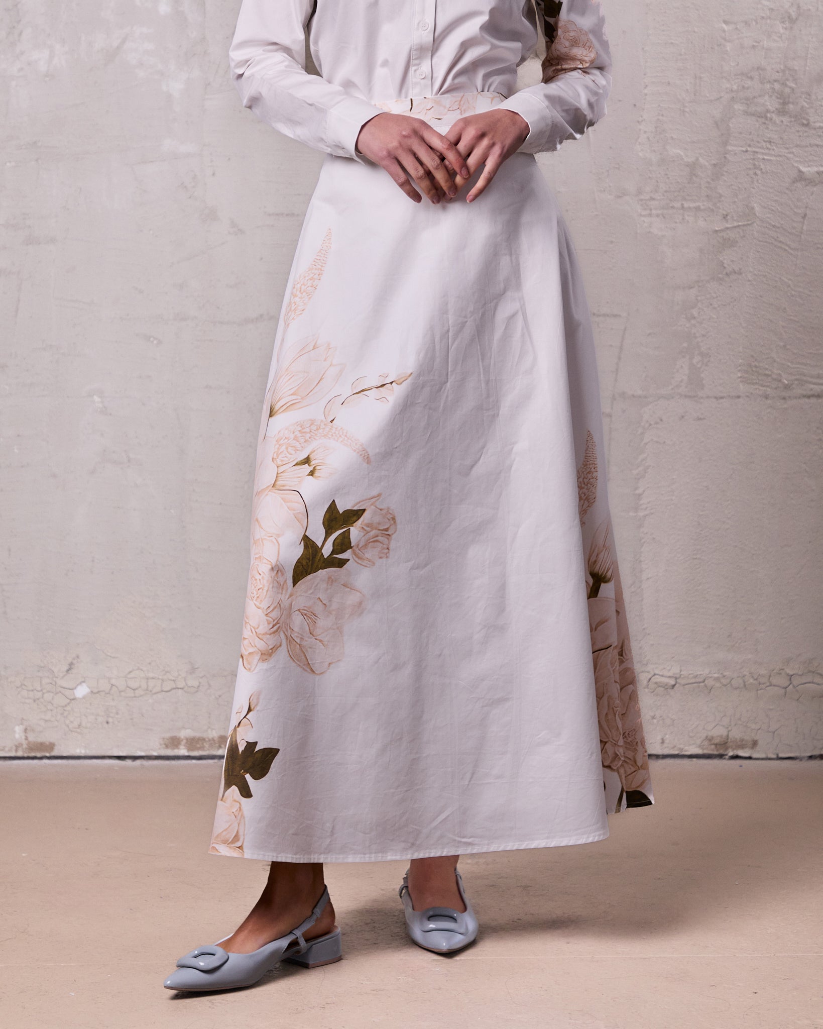 Person wearing a long white dress with floral patterns against a plain background